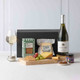 Gourmet White Wine & Cheese Gift Box. A wooden board displays an assortment of cheese, crackers, and fresh grapes. Beside it, a bottle of white wine rests on a light surface. A glass filled with wine stands nearby, with a black gift box in the background. A jar of chutney is also visible on the board. Gourmet White Wine & Cheese Gift Box. A wooden board displays an assortment of cheese, crackers, and fresh grapes. Beside it, a bottle of white wine rests on a light surface. A glass filled with wine stands nearby, with a black gift box in the background. A jar of chutney is also visible on the board.